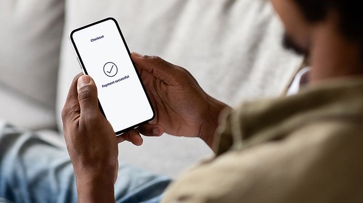 A man is sitting on a sofa holding a smartphone with the words "Payment successful" on the screen