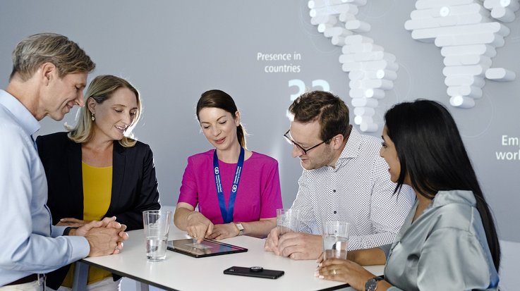 A woman with a G+D lanyard explains something to a group of people on a tablet
