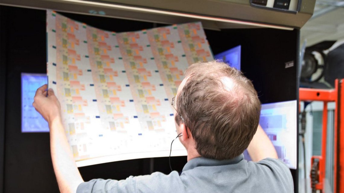 A man holds a sheet of banknotes up to the light and looks at it closely