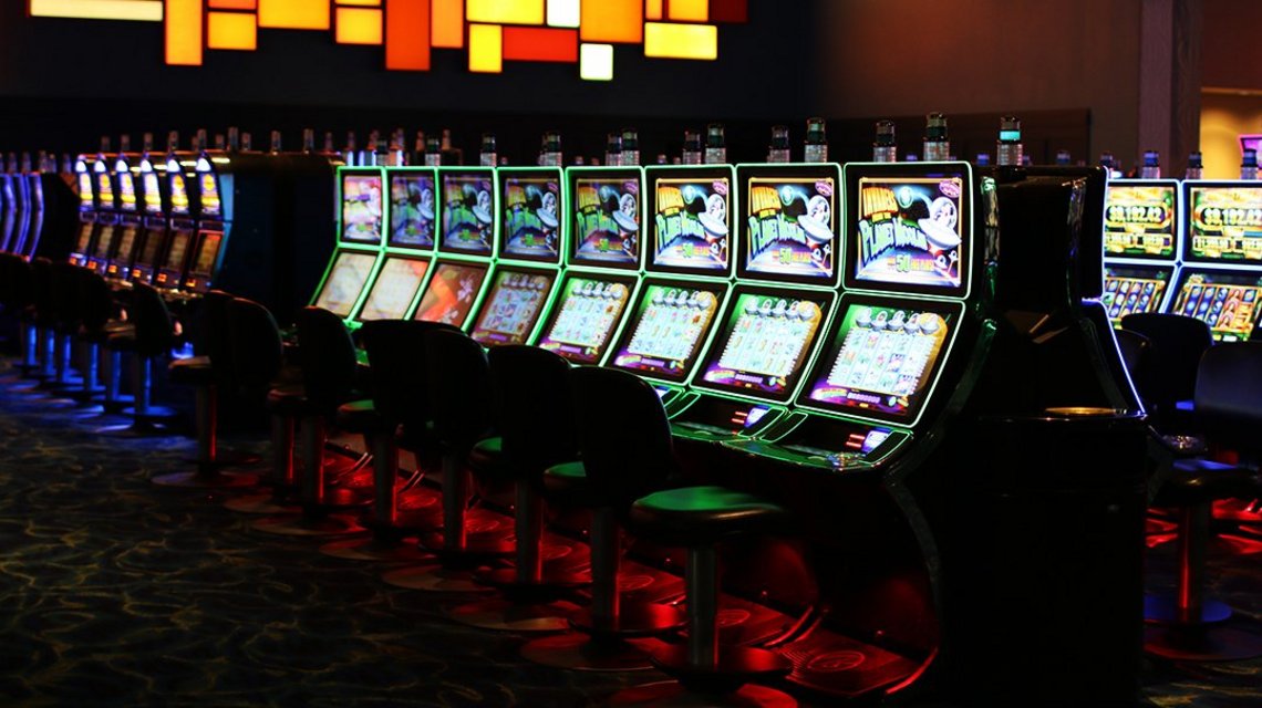 Many slot machines side by side each with a chair in front of it