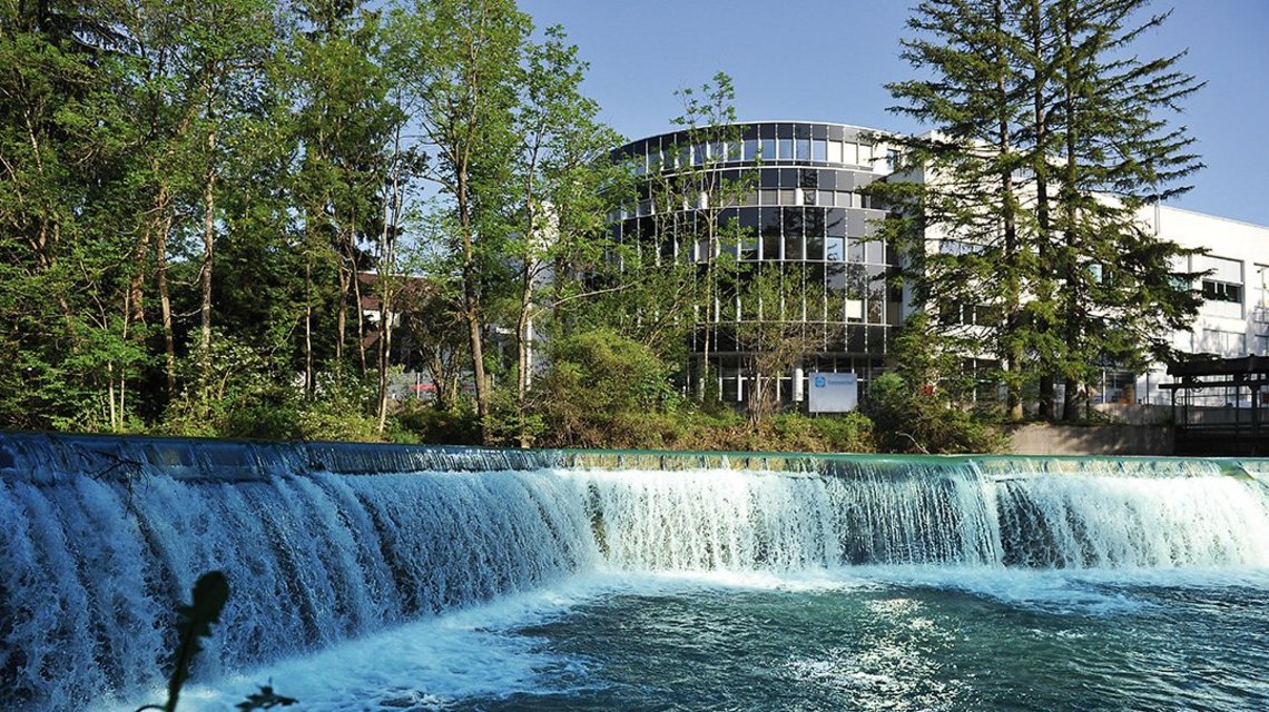 A small waterfall on a wide body of water, in the background an office building