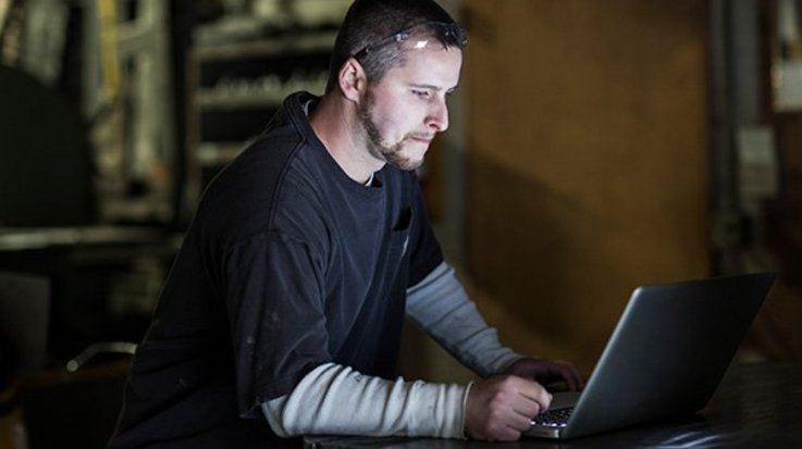 A man with pushed up glasses sits at a laptop and looks at the display