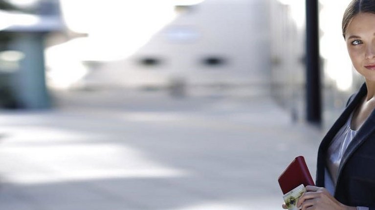 A woman in business attire holds her handbag and a credit card in her hands