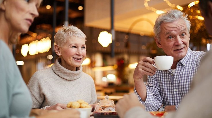 Four elderly people sit together at a table and eat and drink together