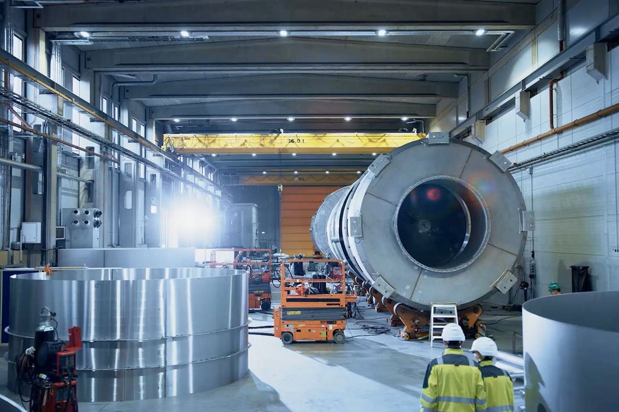 Two people wearing hard hats walk through a production hall for large components