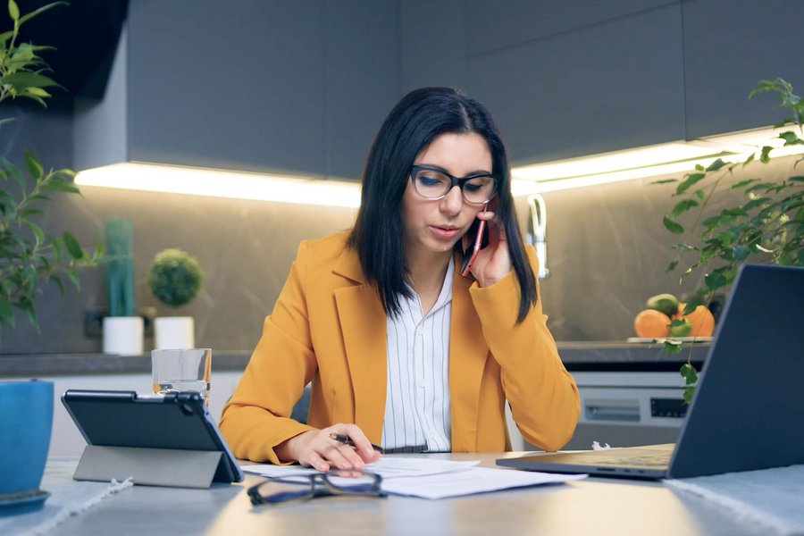 A businesswoman operates her laptop and makes calls on her smartphone in her office at home