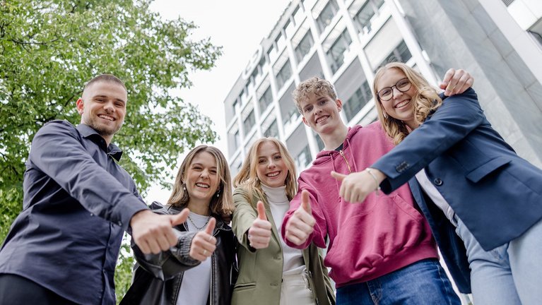 Group of young people giving thumbs up in front of modern building