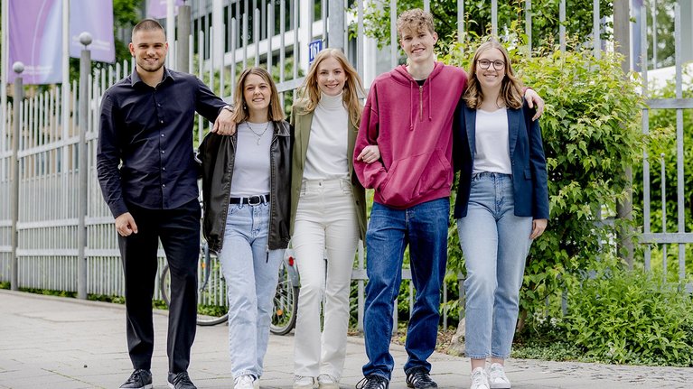Five young people walking arm in arm on the sidewalk