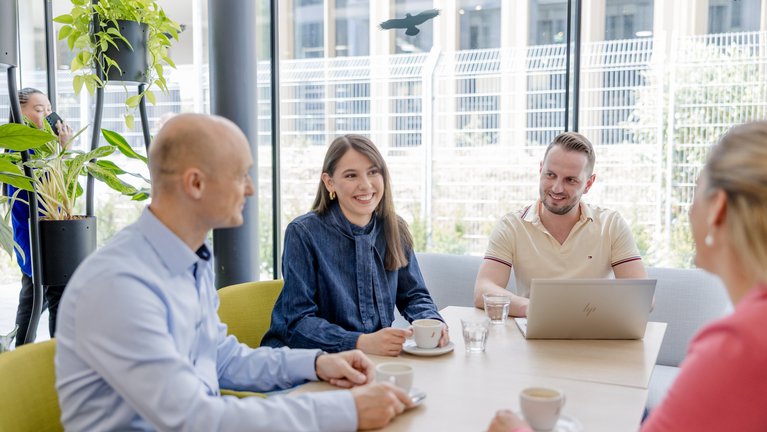Four people sitting with coffee and laptop at a table in the office