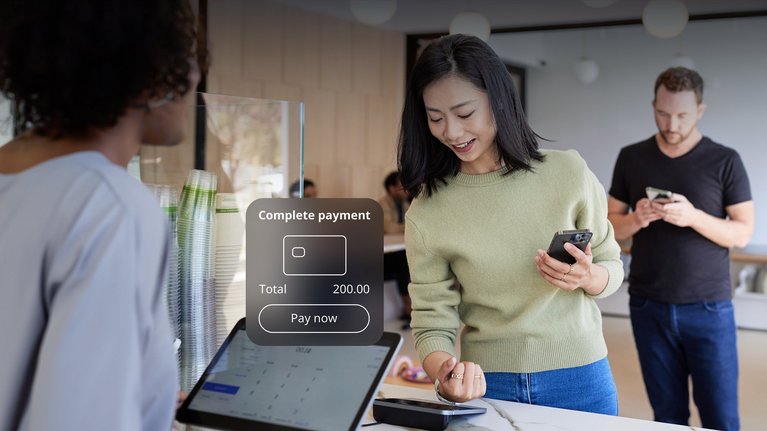 A cafe setting with a customer making a payment at a digital terminal with their smart watch.