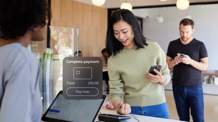 A cafe setting with a customer making a payment at a digital terminal with their smart watch.
