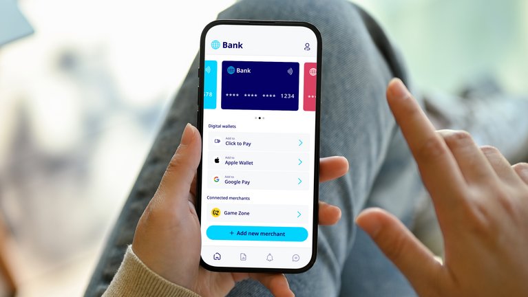 A close-up of a person's hands holding a smartphone displaying a bank app interface with options for digital wallets and connected merchant services.