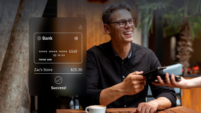 A man completes a contactless payment using a mobile device at an outdoor cafe, with a success message displayed on the payment terminal screen.