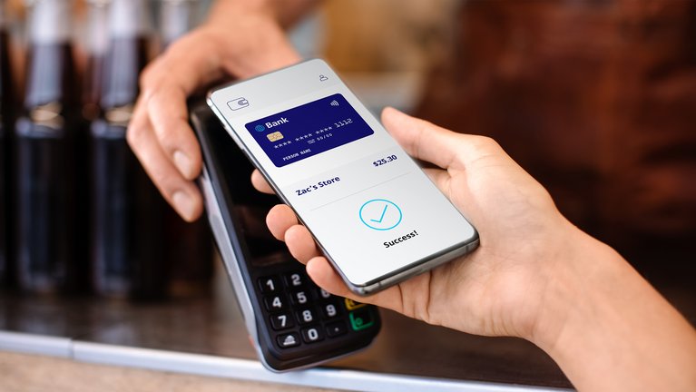A close-up view of a person's hand holding a smartphone displaying a successful payment confirmation screen above a payment terminal.