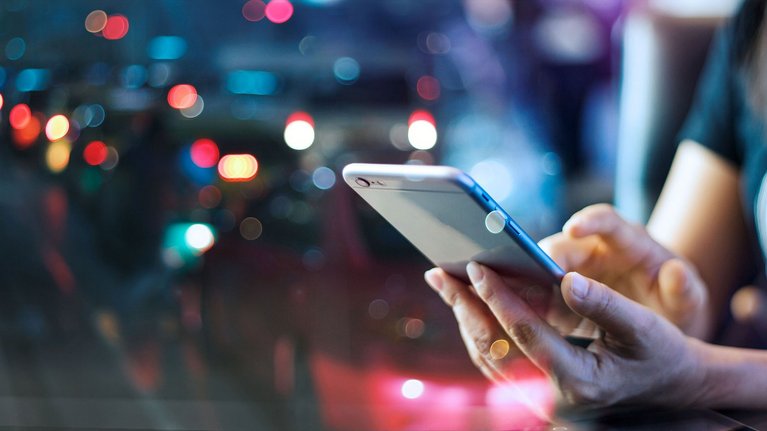 Close-up of hands holding a smartphone with blurred city lights in the background.