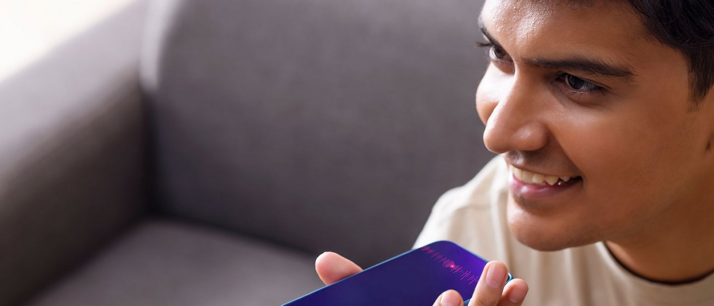 Smiling man using voice command on his smartphone while sitting on a couch.