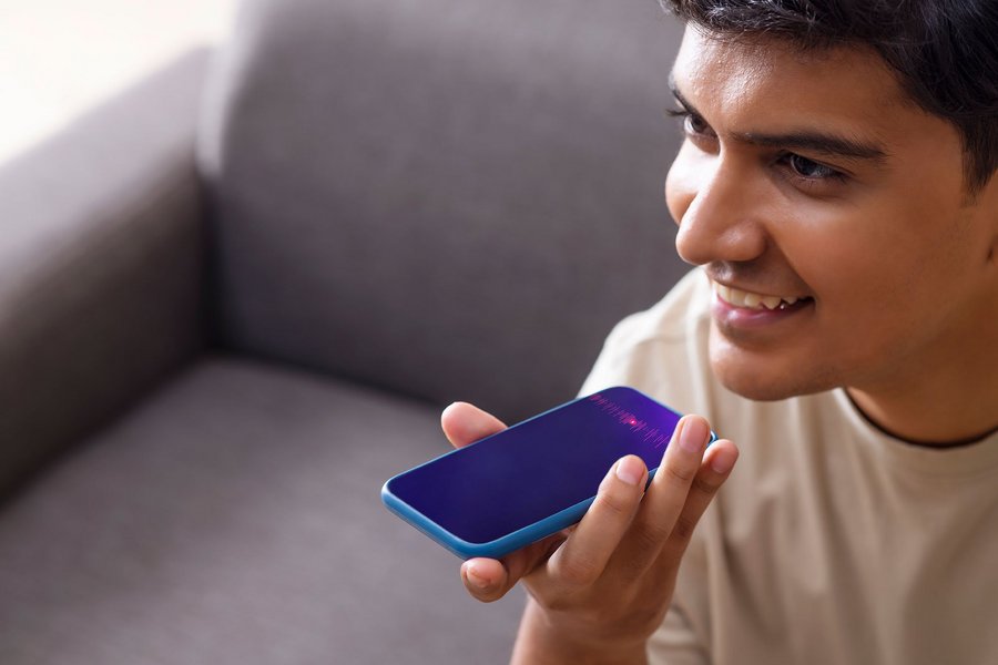 Smiling man using voice command on his smartphone while sitting on a couch.