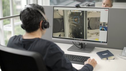 A professional working on a laptop and monitoring machinery repair on multiple screens.