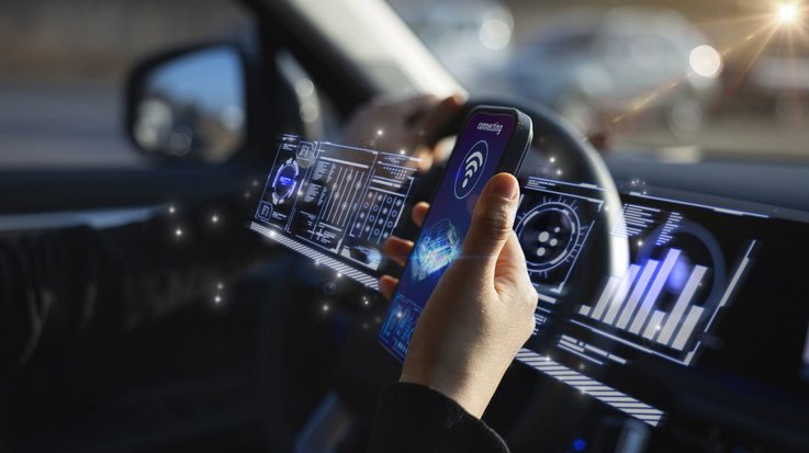 Hand holding smartphone in car with digital displays.