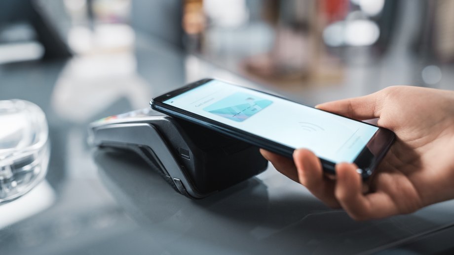 A smartphone is held to a black terminal for contactless payment via wallet.