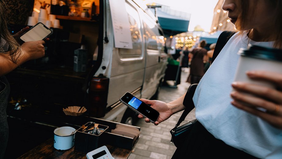 A woman hands her phone to make a payment while purchasing coffee at an outdoor coffee truck