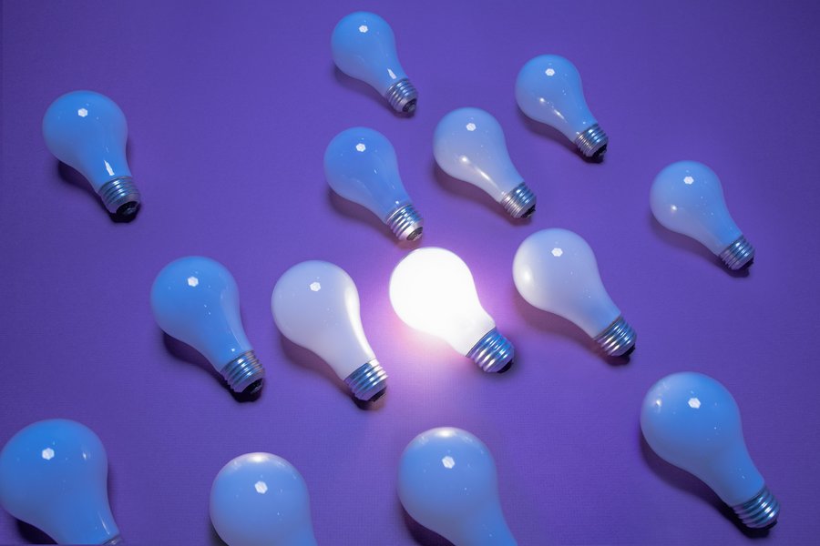 Several Lightbulbs laying on purple Background, one is glowing