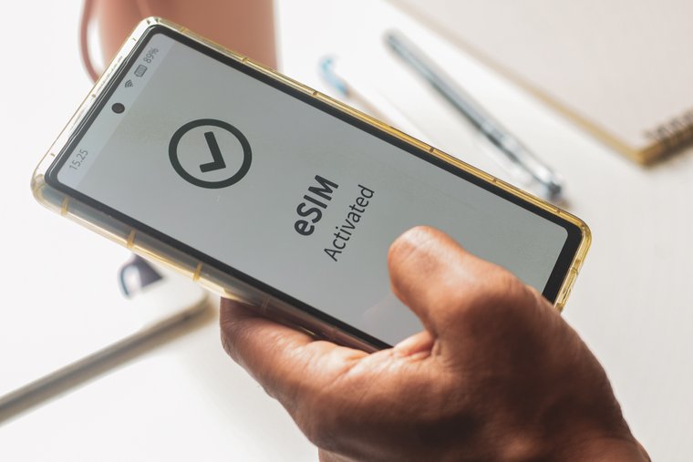 A hand holds a smartphone with eSIM activation screen displayed.