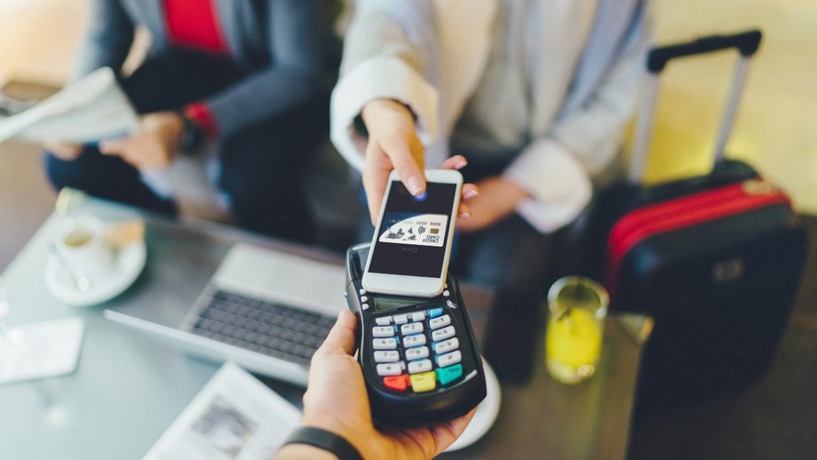 Person making a contactless payment with a smartphone on a card reader in a modern setting.