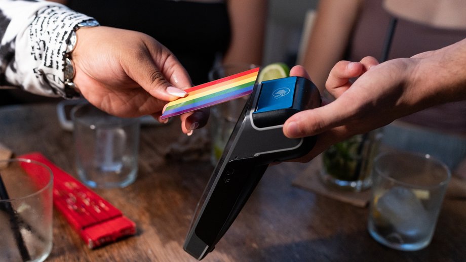 A woman makes a contactless payment with her colorful credit card at a card terminal.