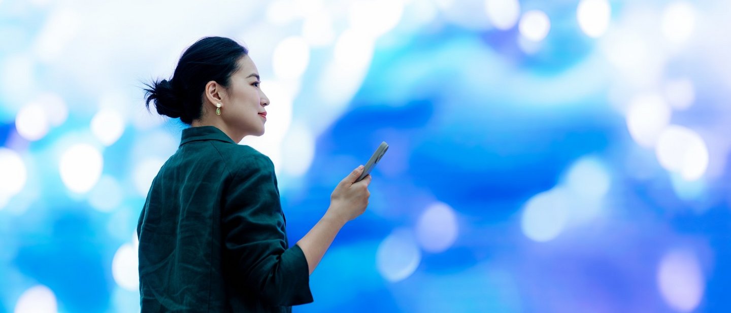 Asian businesswoman with smartphone standing in front of a big screen, doing an instant payment