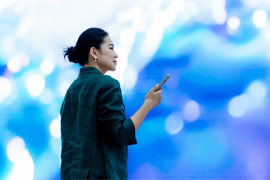 Asian businesswoman with smartphone standing in front of a big screen, doing an instant payment