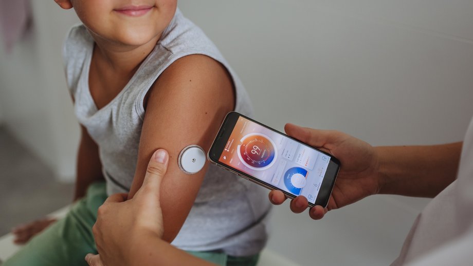 Boy with health sensor on arm connected to a smartphone app displaying vital data.