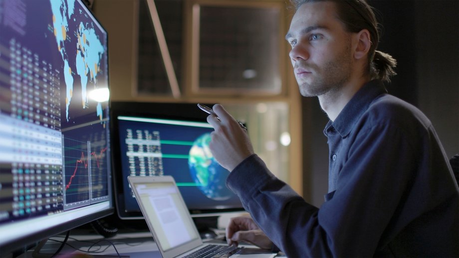 Analyst reviewing IoT data on screens in a modern control room with a world map