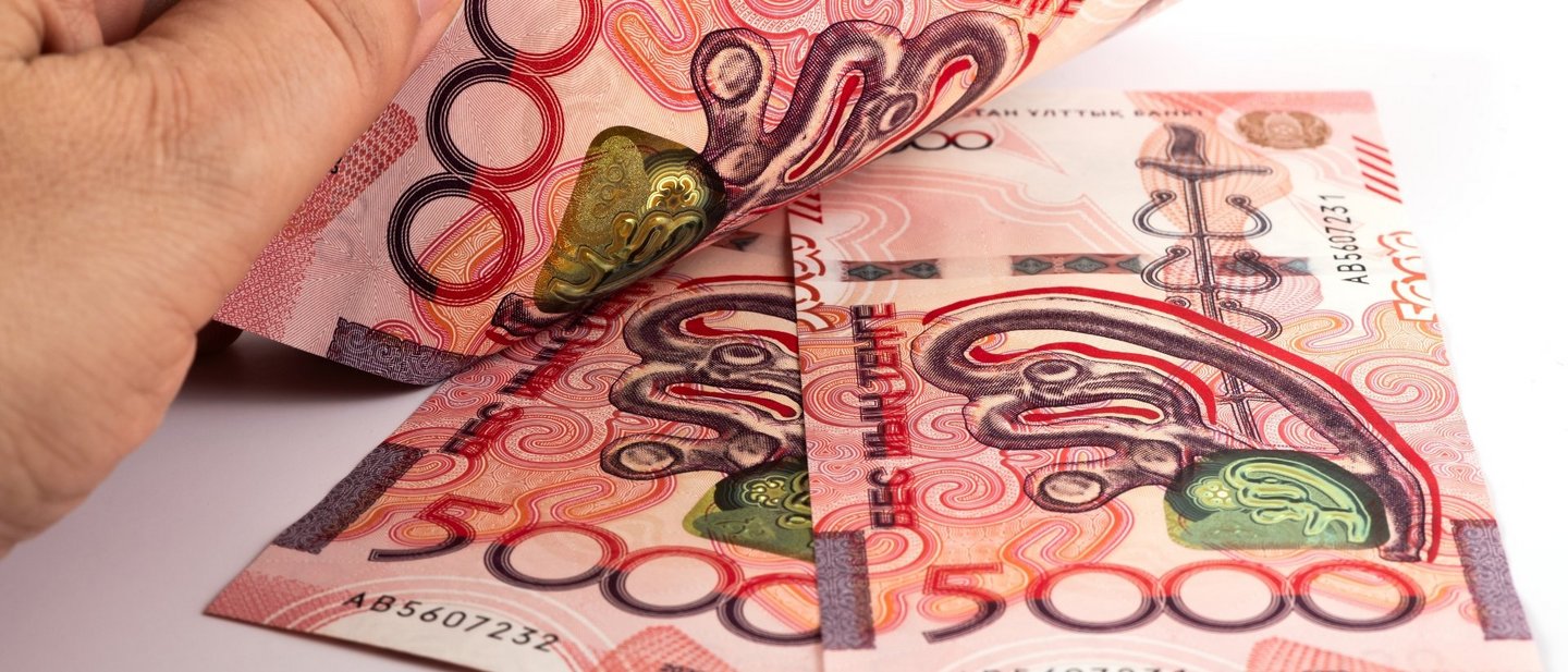 Three red new Kazakh 5000 Tenge banknotes with a man’s hand on them.