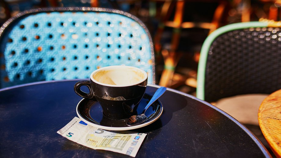 Empty cup of black coffee and five euro banknote as a tip on a table of an outdoor café.