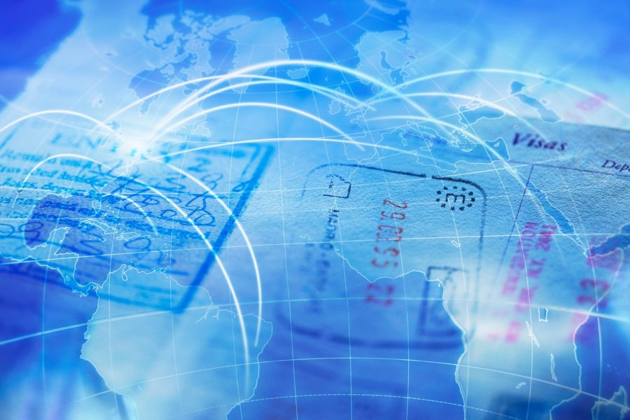 A passport full of different stamps lies on a blue colored world map with travel destinations.