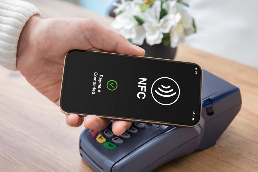 Male hand holds a smartphone to a pos terminal in order to pay via wireless technology (NFC)