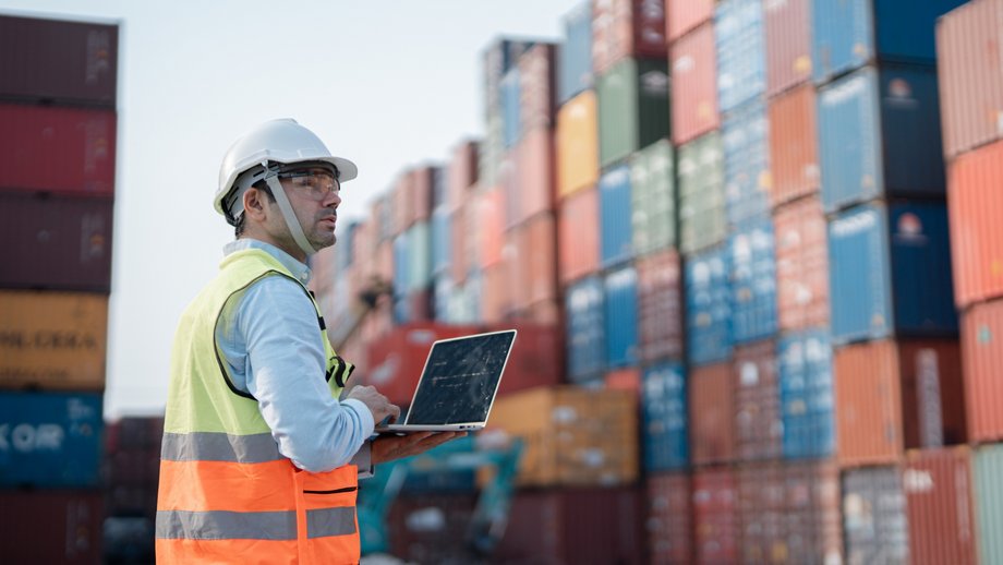Engineer with laptop in front of container stack