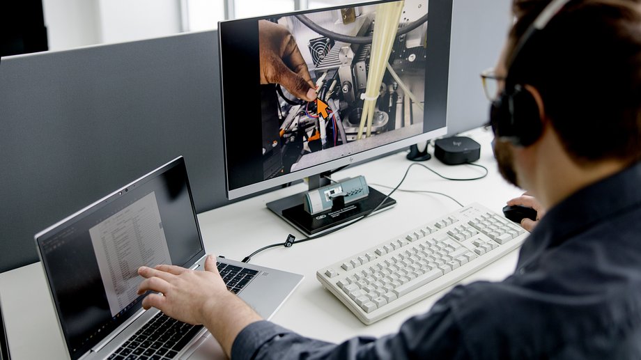 Technician with a headset works on a laptop and watches a technical video transmission on a monitor
