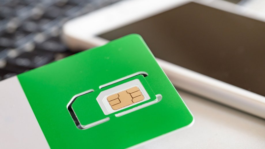 Green SIM card partially removed from holder, with white smartphone in background.