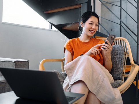 Person sitting in chair using smartphone next to laptop