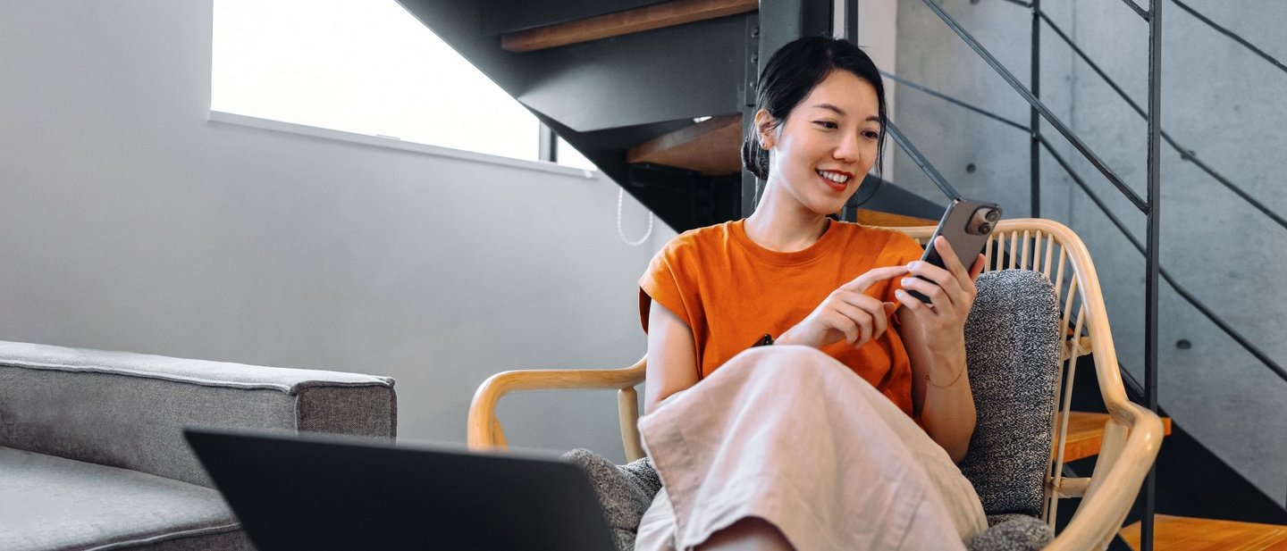 Person sitting in chair using smartphone next to laptop