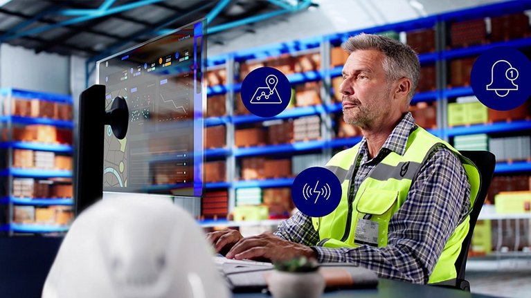 Picture of a warehouse worker in a high-visibility vest checking a tracking dashboard on a digital screen