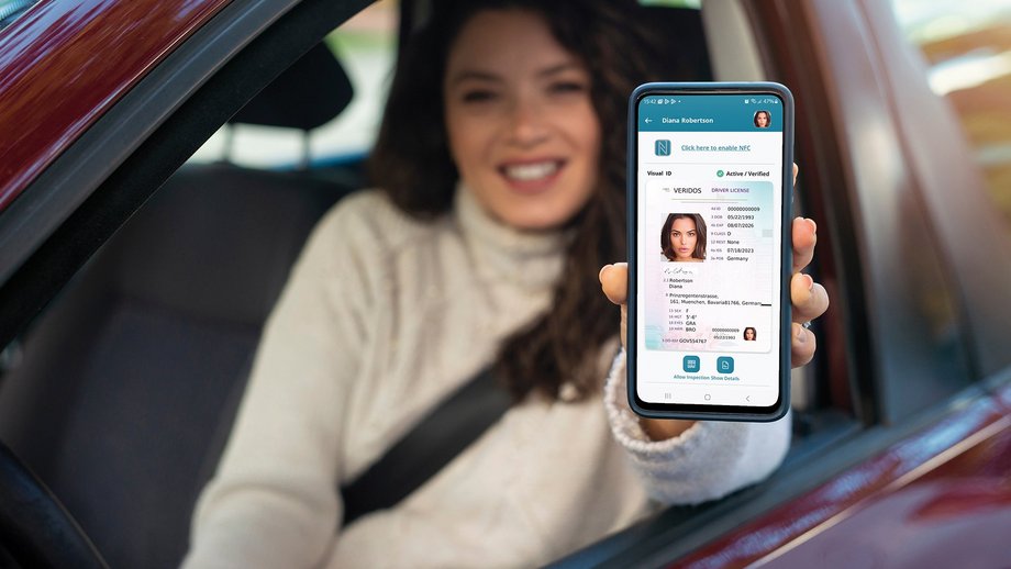 A person in a car holds a smartphone displaying a digital driver's license with personal details.