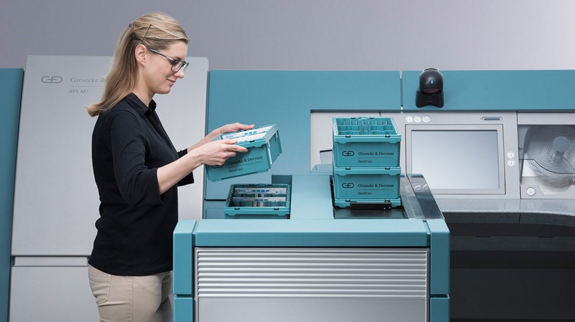 A woman stacks NotaTrays filled with banknotes on top of each other