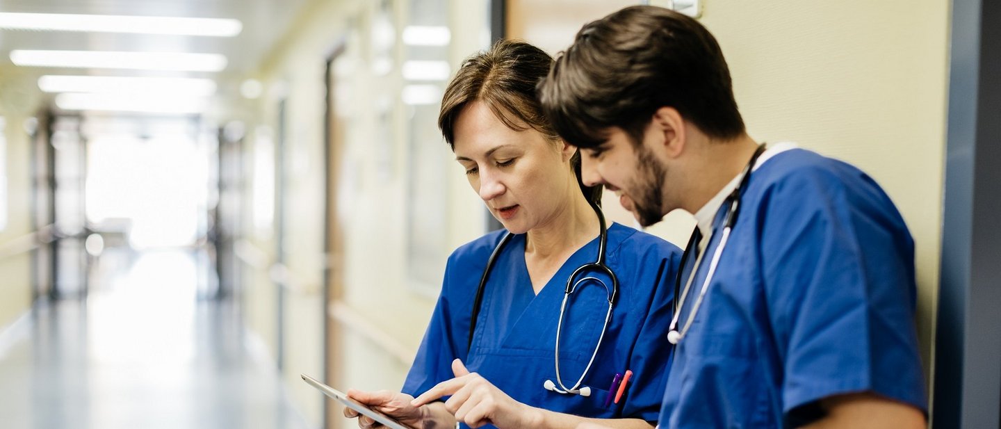 Two medical staff look at a tablet in a medical setting.