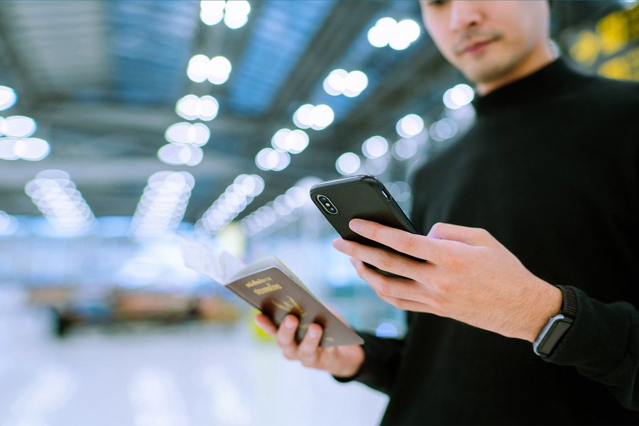A man stands in an airport holding his smartphone in one hand and his passport in the other