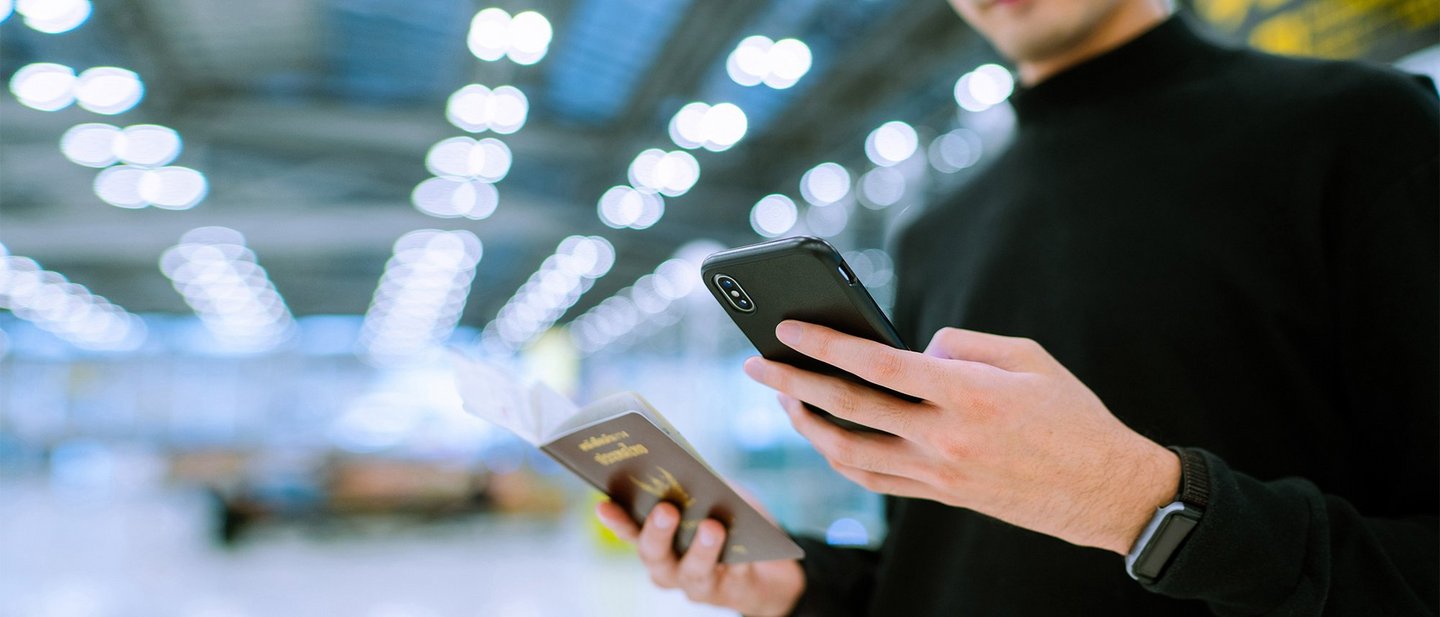 A man stands in an airport holding his smartphone in one hand and his passport in the other