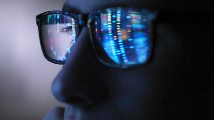 A luminous screen is reflected in the glasses of a man