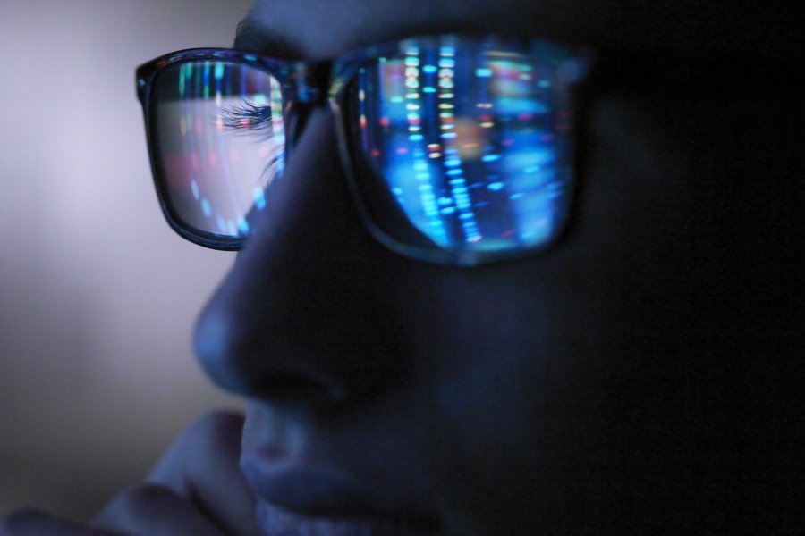 A luminous screen is reflected in the glasses of a man